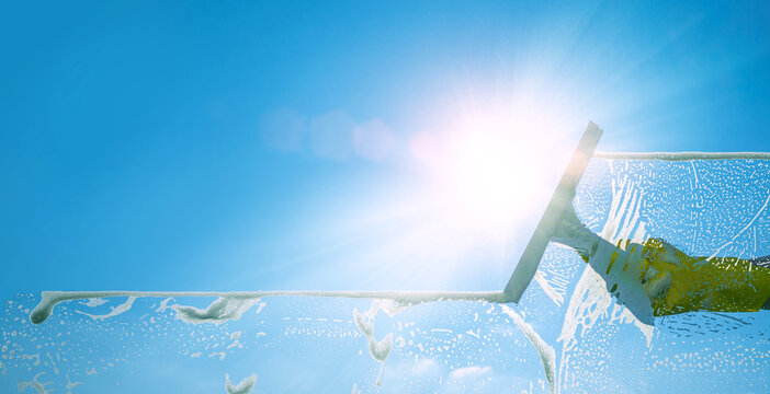 Window Cleaner Cleaning Window With Squeegee And Wiper On A Sunny Day With A Bright Blue Sky