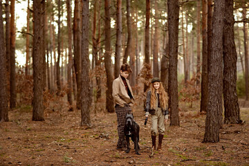 Fototapeta premium Girl and boy walk with a dog Cane corso in the forest and have a fun. Children stand near a tree and hold a dog on a leash.