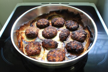 Homemade burgers in a baking pan on a ceramic kitchen cooktop ready to eat. Selective focus