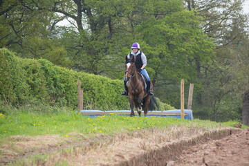 Rider and horse moving at speed away from a jump they have just jumped outdoors in the English countryside of rural Shropshire.