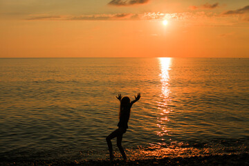 Happy girl dancing at sunset beach with raised arms. Selective focus.