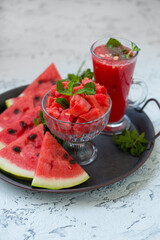 Pieces of ripe watermelon and a glass of watermelon juice on a dish and a light texture background.