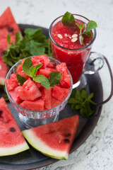 Pieces of ripe watermelon and a glass of watermelon juice on a dish and a light texture background.