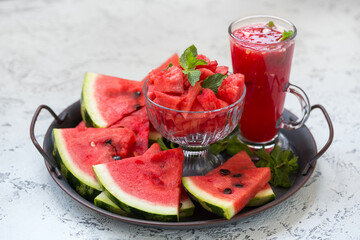 Pieces of ripe watermelon and a glass of watermelon juice on a dish and a light texture background.
