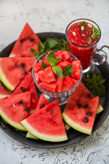Pieces of ripe watermelon and a glass of watermelon juice on a dish and a light texture background.