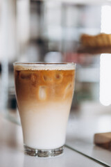 Glass with coffee, milk and ice on cafe background