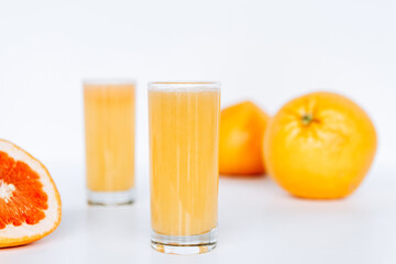 Glass with grapefruit juice and whole and sliced grapefruit on the background