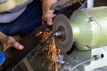 Blacksmith's hands sharpening a carpenter's saw using a bench grinder
