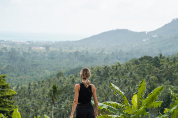 Back side of woman in black t-shirt enjoying tropical forest view with mangrove trees. Mountains...