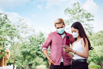 Couple in Face Mask in Public Park. Young Man and Woman Wear Facemask to Prevention in Coronavirus or Flu Outbreak. New Normal , Social Distancing , Healthcare Concept