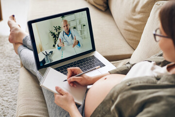 Professional doctor on laptop display consulting young pregnant woman