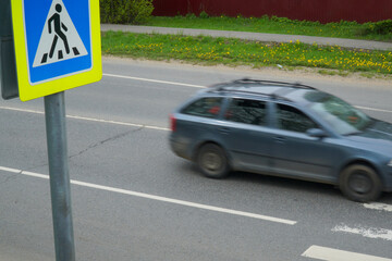   Sign of the transition on the background of a passing car. Road crossing danger concept at unregulated pedestrian crossing.