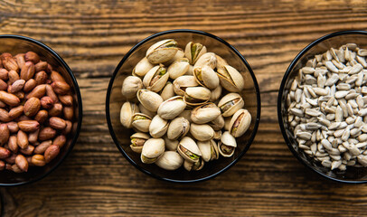 Sunflower seeds, pistachios and peanuts in a small plates which standing on a wooden vintage table. Nuts is a healthy vegetarian protein and nutritious food. Nuts on rustic old wood.