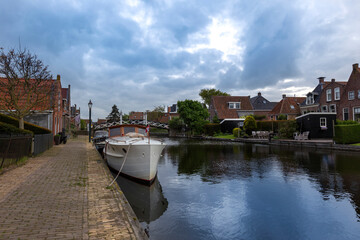 Obraz premium Netherlands - Hindeloopen a water canal on which a white ship is moored. Traditional Dutch family houses stand on the sides of the canal. In the background you can see a wooden bridge