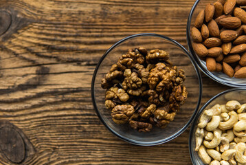 Almond, walnut and cashew in a small plates which standing on a wooden vintage table. Nuts is a healthy vegetarian protein and nutritious food. Nuts on rustic old wood.