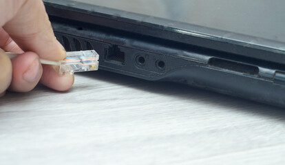 A man inserts an Internet cable into the laptop's network port. closeup.
