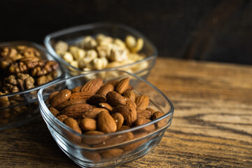 Almond, walnut and cashew in a small plates which standing on a wooden vintage table. Nuts is a healthy vegetarian protein and nutritious food. Nuts on rustic old wood.