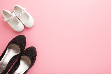 Mother black shoes and daughter white sandals on light pink table background. Pastel color. Empty place for text. Top down view.