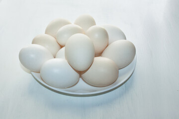 Huge white chicken eggs stacked in a white plate on a white background.