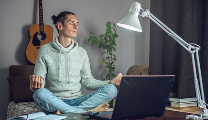 Employee is meditating in the Lotus position while working hard remotely at home. Calm and serenity during a crisis