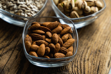 Almond, pistachio and sunflower seeds in a small plates which standing on a wooden vintage table. Nuts is a healthy vegetarian protein and nutritious food. Nuts on rustic old wood.