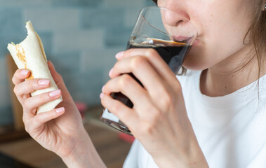 Woman drink cola and eat kebab. A beautiful girl bites a chicken roll close up. Delicious and harmful fast food