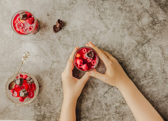 Young woman hands holding and eating jelly dessert with fresh raspberries served in glasses on gray background. Top view. Healthy lifestyle and summer or diet food concept