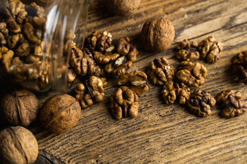 Walnut scattered on the vintage table from a jar whith a whole walnuts. Walnut is a healthy vegetarian protein nutritious food. Walnut kernels and whole walnuts on rustic old wood.