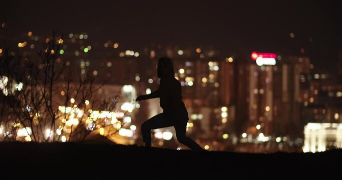 Silhouette of a male dancer dancing in the night up in the hill in front of the city lights