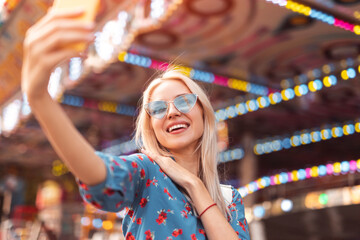 Cheerful young woman taking selfie with smartphone in amusement park