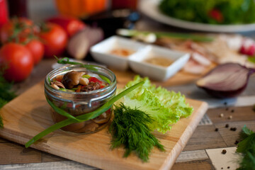 pickled mushrooms in a transparent jar on a wooden Board on the table with vegetables