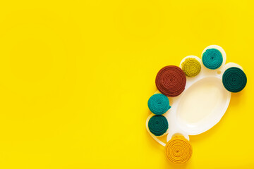 Paint palette with rolls of fabric stripes as a paint on an yellow background. The fabric stripes are made of old wears. The concept of upcycling and zero waste.