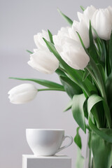 Fototapeta na wymiar A huge bouquet of white fresh tulips in vase near a cup of coffee closeup. Romantic spring morning, breakfast in bed. Shallow depth of field.