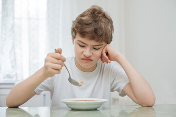 The boy sits at the table in front of a plate of porridge. He doesn't want to eat.