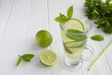 Infused water or cold lemonade with lime, ice and  mint  in the glass  on the white wooden  background. Copy space.