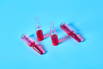 Glass capsules with red vaccine on blue background. Healthcare and medical concept