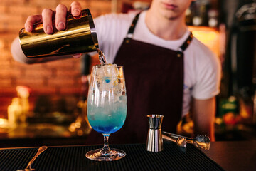 Barman preparing at the bar counter Blue Lagoon cocktail close-up, ice cubes and soda bubbles