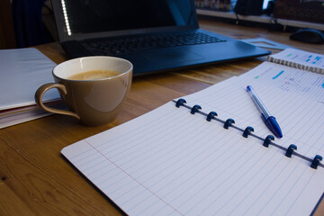 Wooden table, laptop, coffee and notebook with blue pen; study, work from home online.