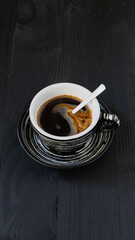 Dark cup of black coffee on a black background. Minimalism. Vertical orientation.