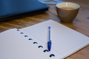Wooden table, laptop, coffee and notebook with blue pen; study, work from home online.