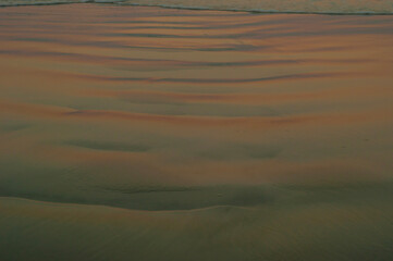 Water reflections on wet sand at sunset