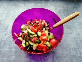 summer vegetable salad tomatoes cucumbers onions green radishes in a purple bowl on a background and a spoon