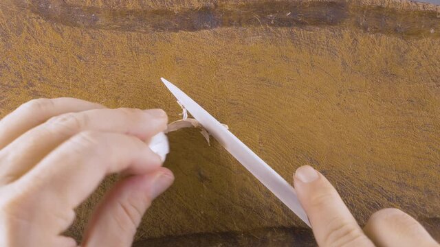 Male cheff hands cutting garlic with a large white ceramic knife on a wooden cutting board. Top Upper View Shot.  Close-up chef shreds garlic on the wooden board. Knife cut a piece from garlic