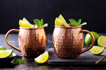 Moscow Mules cocktail with ginger beer, vodka, lime and mint. Grey background. Close up.