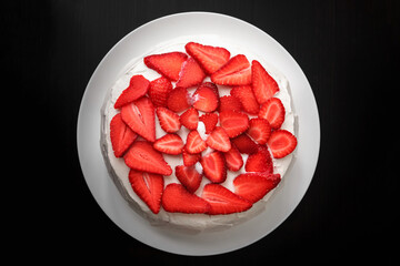 strawberry cake with cream in a white plate on a black wooden table background