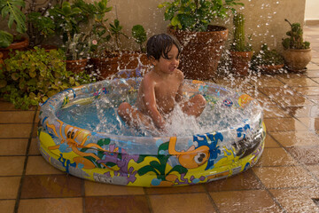 Boy splashing and playing in the inflatable pool. Summer and vacation at home. Lifestyle