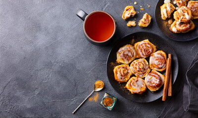 Cinnamon rolls, buns on black plate with cup of tea. Dark background. Copy space. Top view.