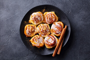 Cinnamon rolls on black plate. Dark background. Close up. Top view.