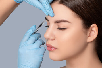 Cosmetologist does injections in the wrinkles between the eyebrows and on the face of a beautiful...