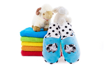 Cute bathroom set. A toy sheep on a stack of colorful towels and slippers isolated on white background.